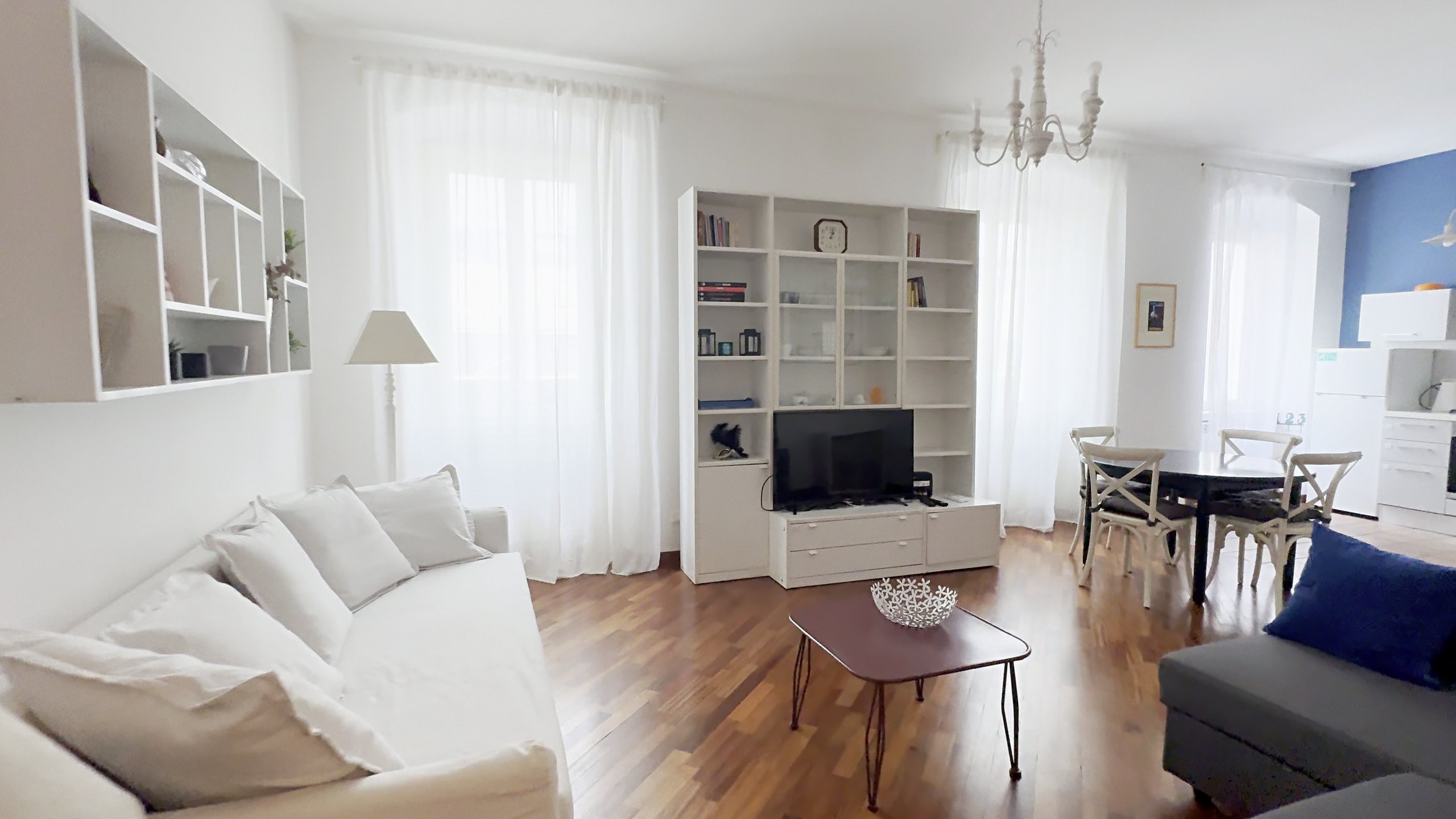 Helles Wohnzimmer mit weißem Sofa, Bücherregal mit TV und Vorhängen, Wohnung in der Via Machiavelli, Triest