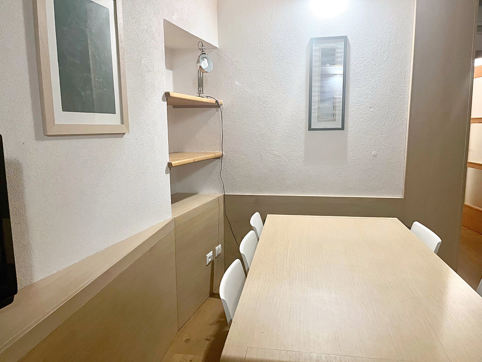 Zona pranzo del soggiorno con tavolo in legno chiaro, sedie bianche e nicchia con mensole, via dei Capitelli, Trieste