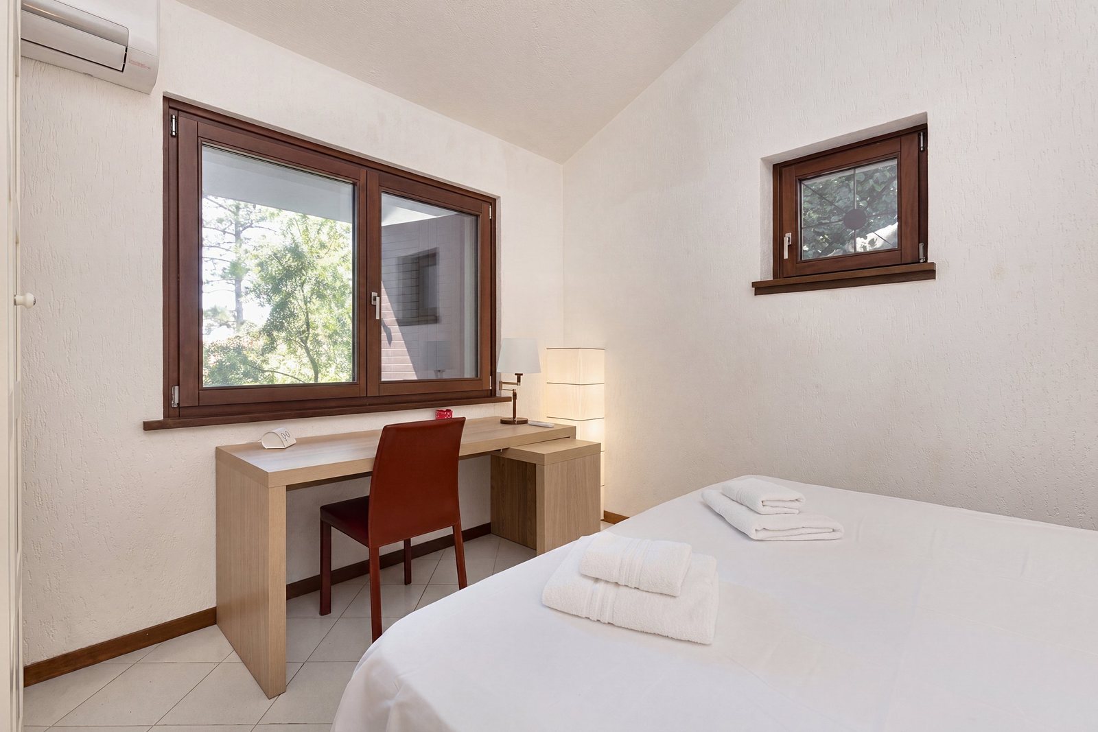 Double bedroom with desk, red chair and window onto the greenery