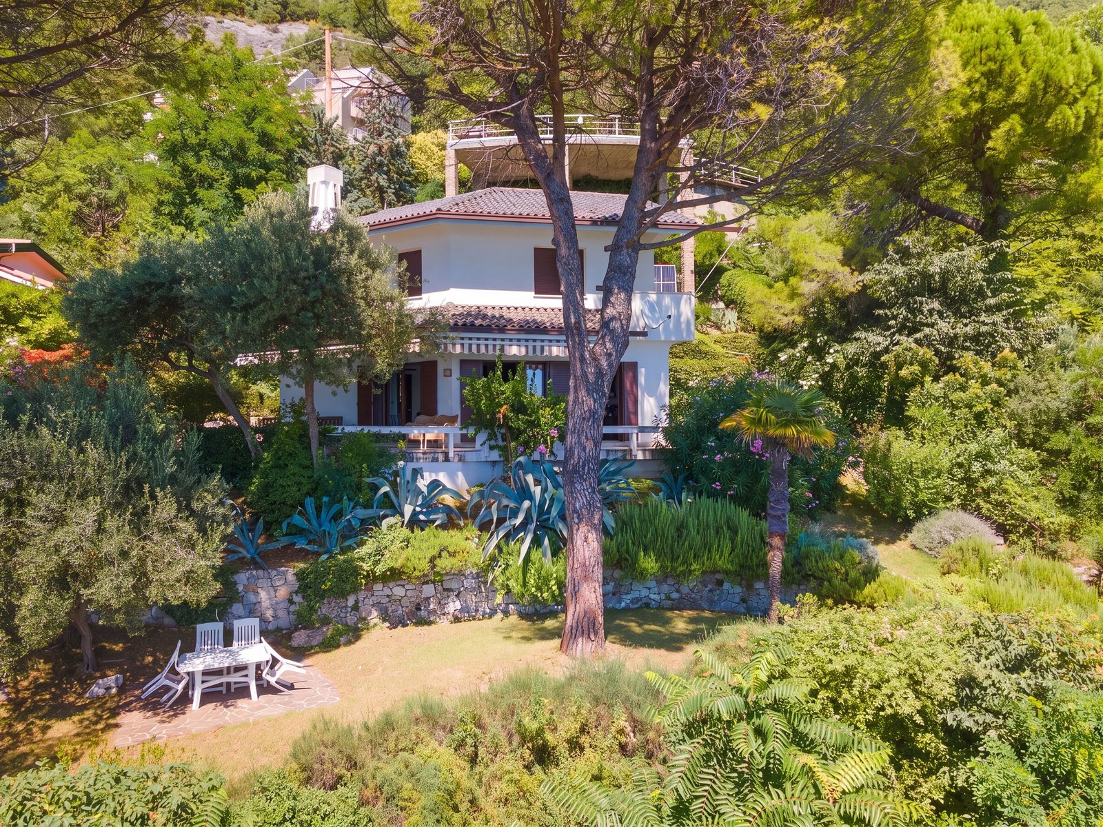 White two-storey villa among pines and agaves, with terraced garden and outdoor table, Aurisina Mare