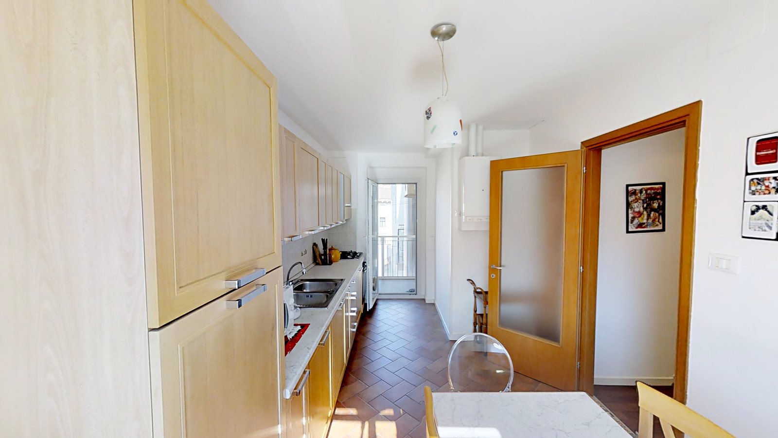 Lange Küche mit terrakottafarbenem Boden und offener Tür zum Balkon, Via Slataper, Triest
