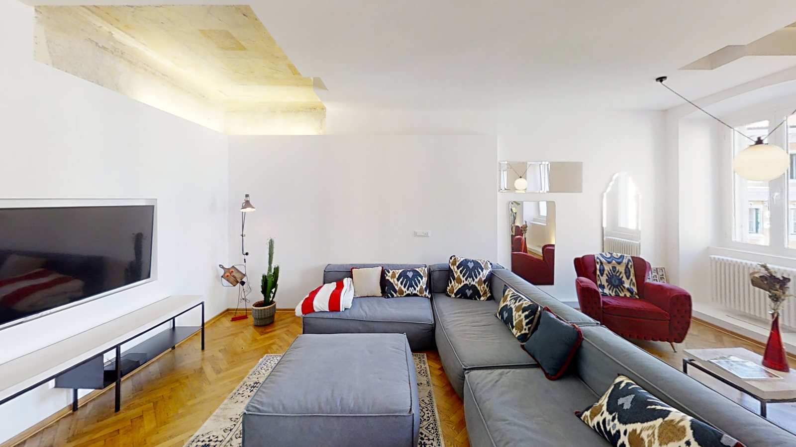 Wohnzimmer mit großem Fernseher, grauem Sofa mit Hocker und rotem Samtsessel, Via dei Fabbri, Triest