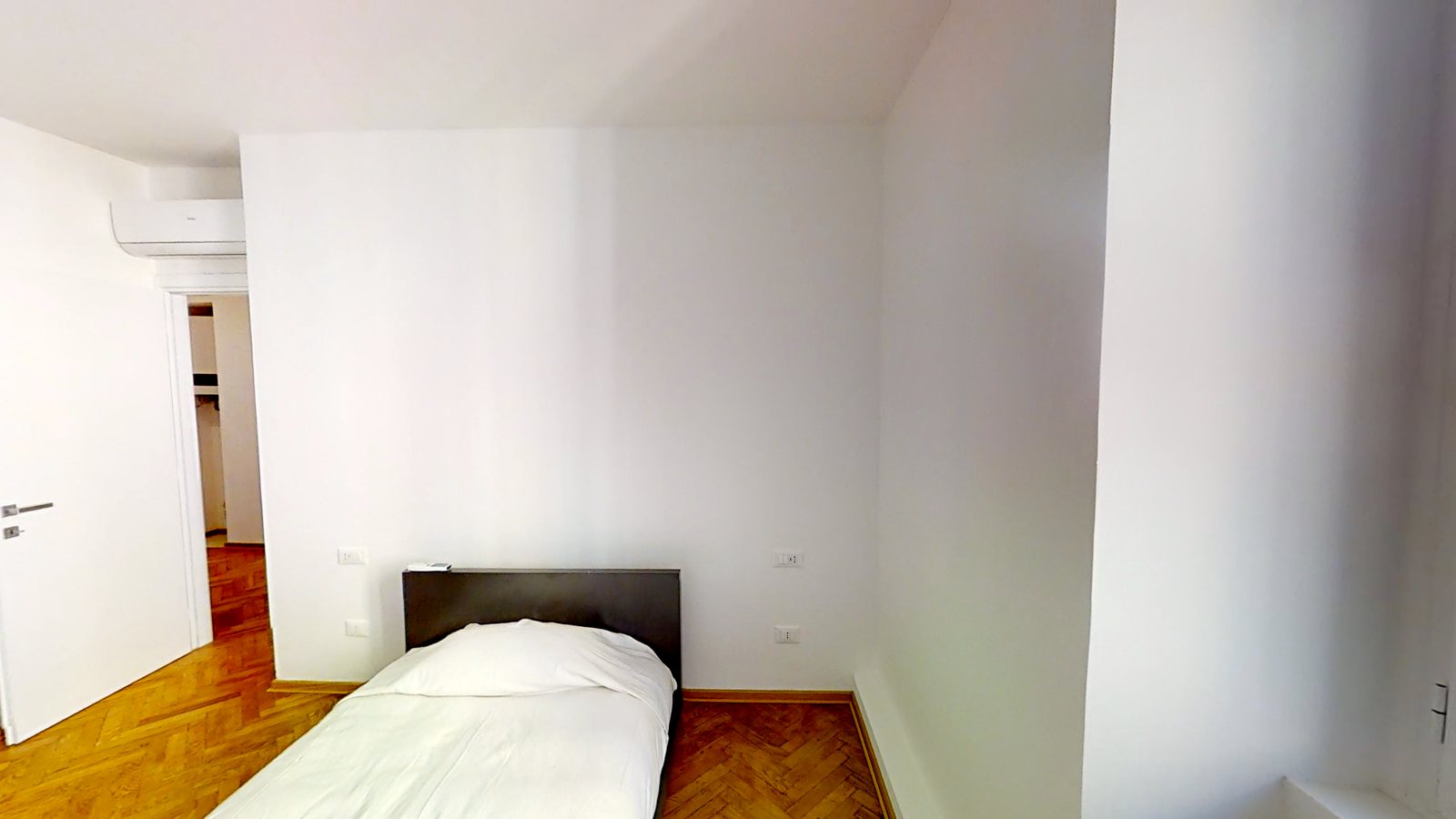 Zweites Schlafzimmer mit Bett mit dunklem Kopfteil, Tür und Fischgrätparkett, Via dei Fabbri, Triest
