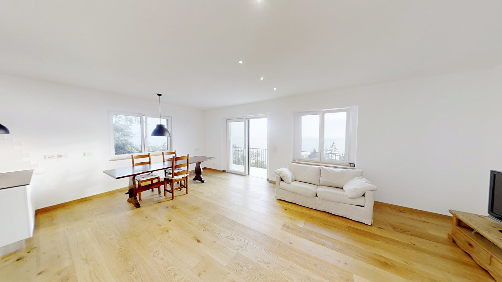 Open-plan living area with dining table, sofa and three openings towards the sea, Salita di Cedassamare, Trieste