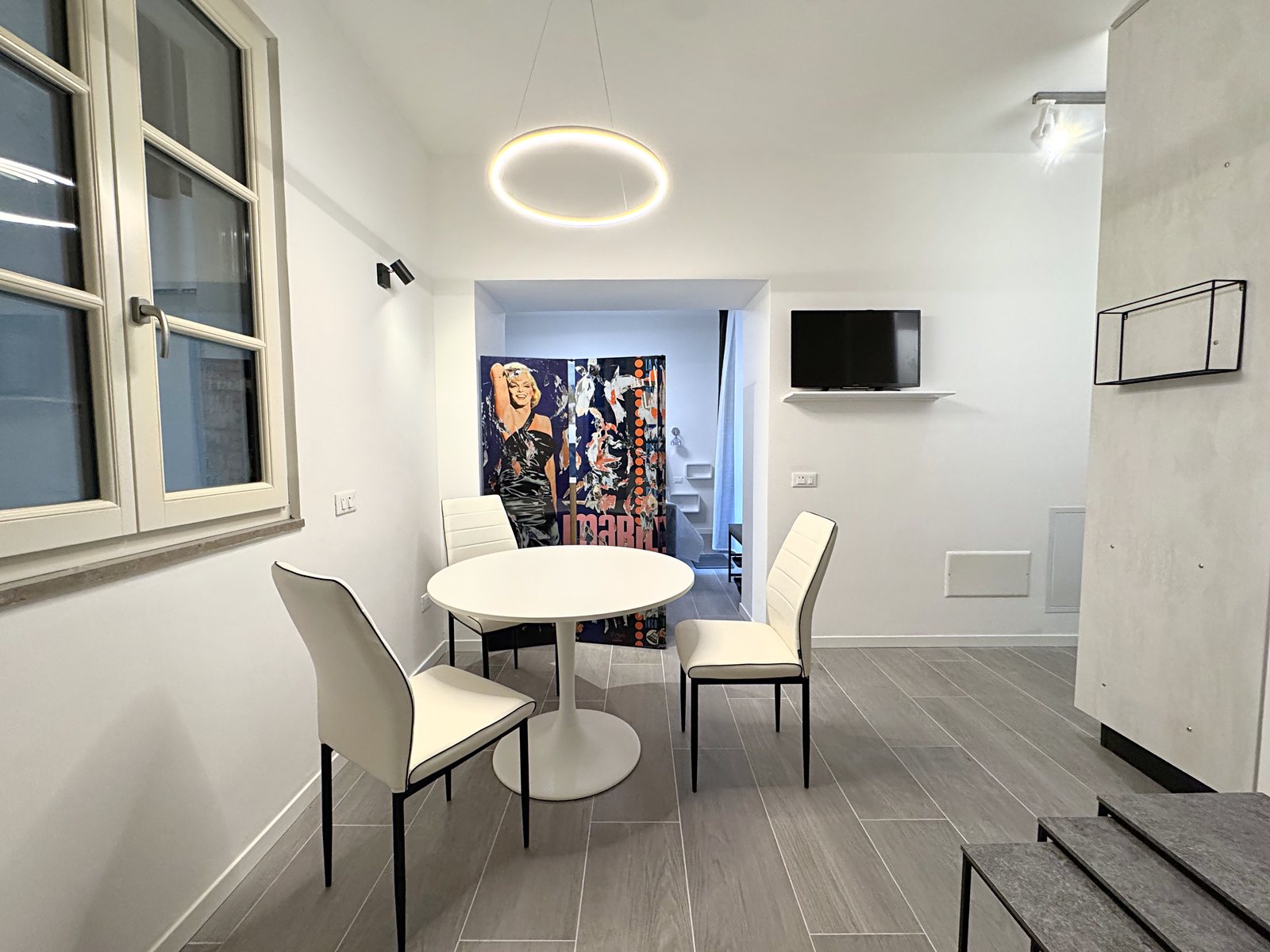 Dining corner with round white table, window and wall-mounted TV, flat in Via del Lavatoio, Trieste
