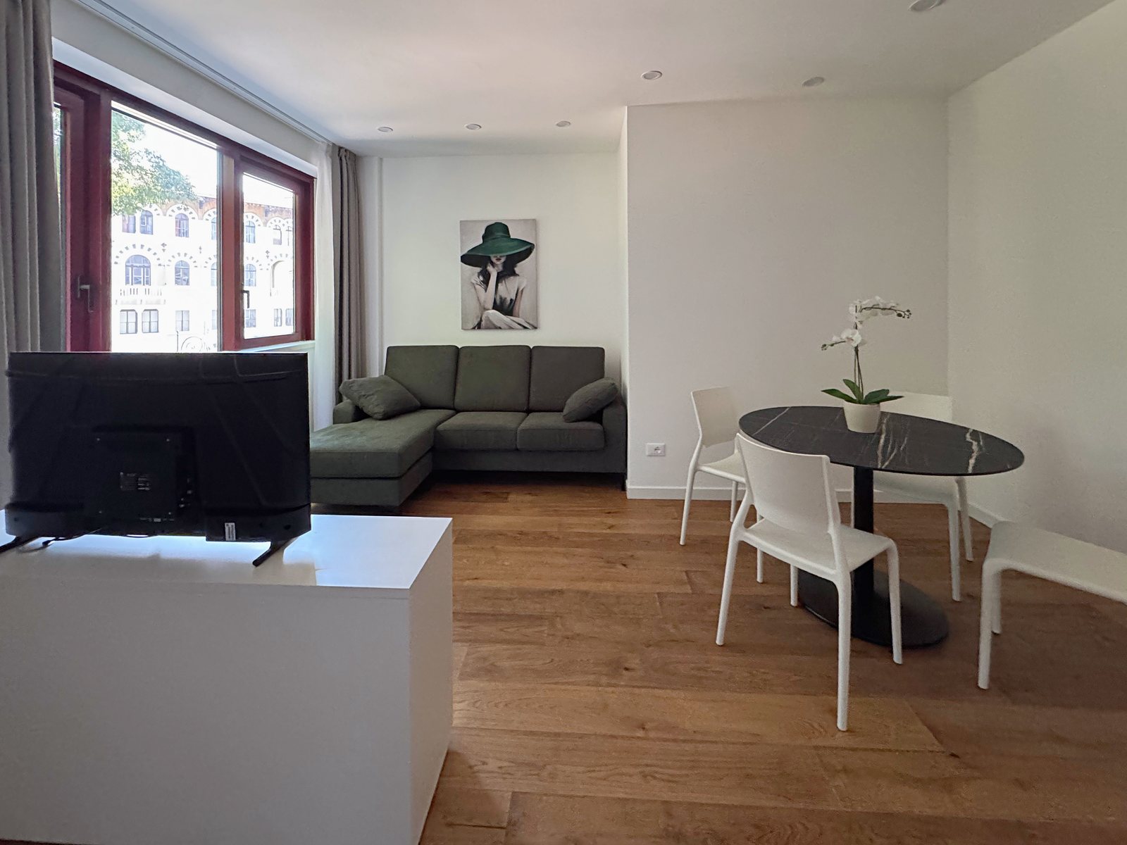 Soggiorno con divano angolare verde, tavolo rotondo e finestra sui palazzi di fronte, via Marconi, Trieste
