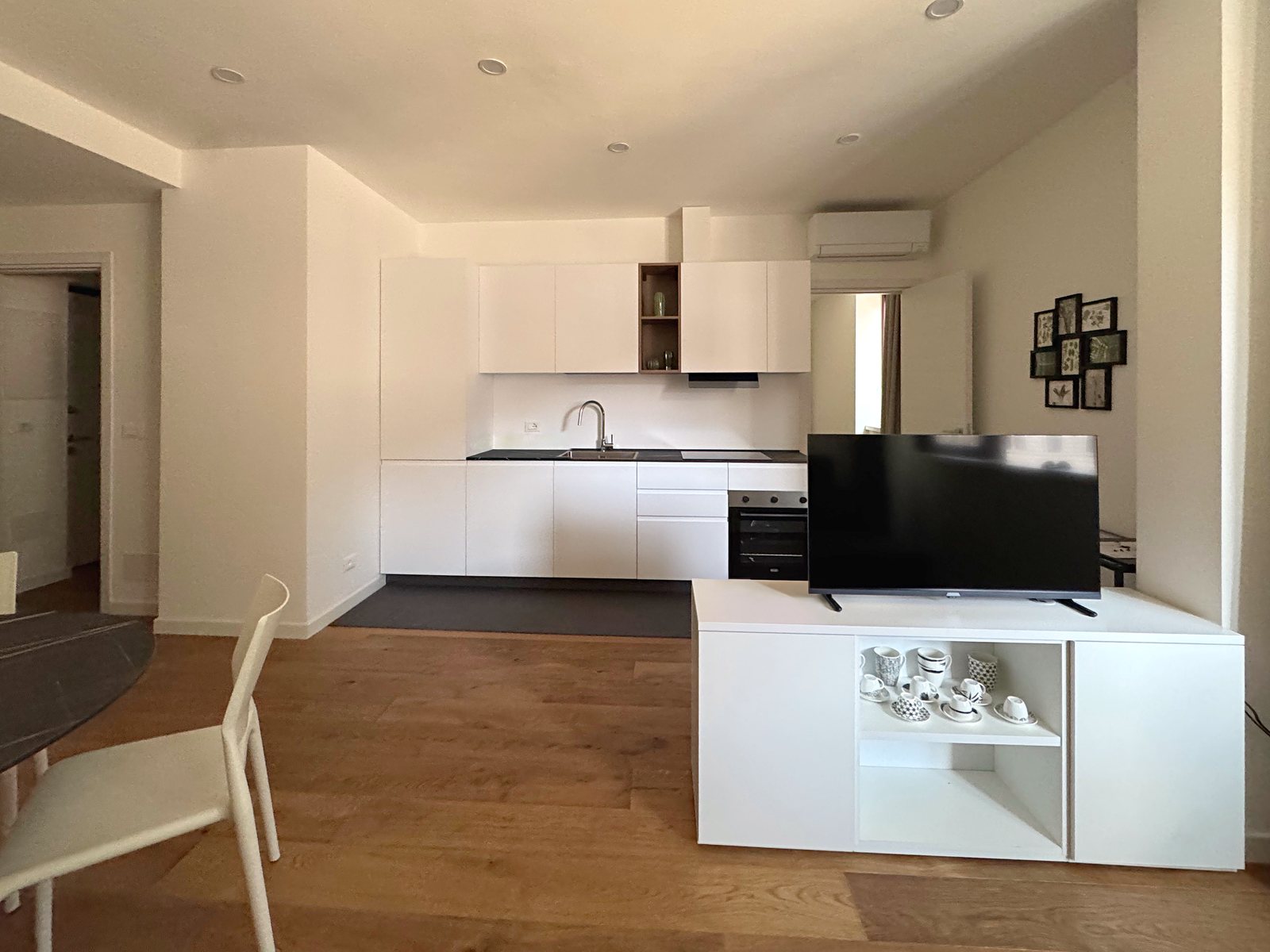 Cucina lineare bianca con piano nero e forno, mobile TV in primo piano, via Marconi, Trieste