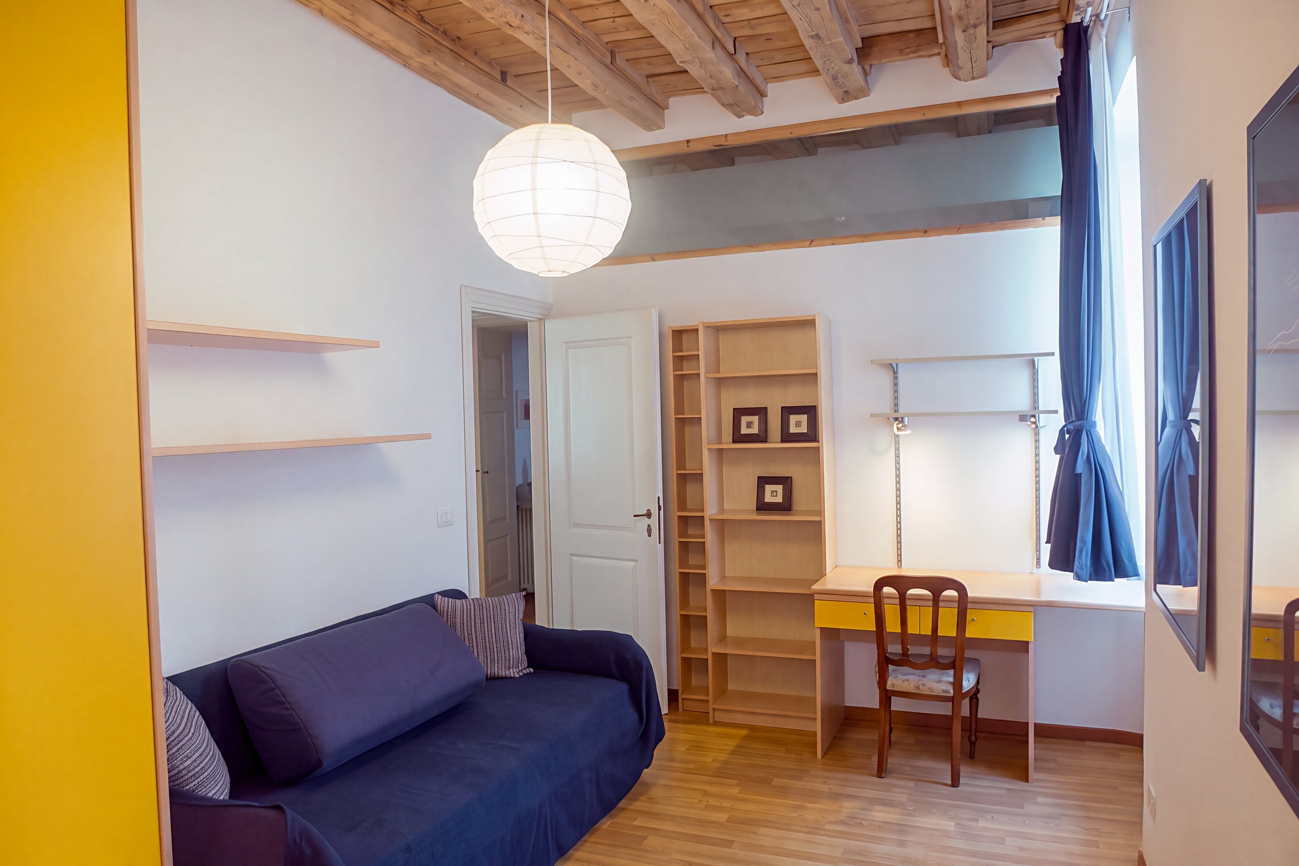 Arbeitszimmer mit Holzbalkendecke, blauem Schlafsofa und gelbem Schreibtisch, Viale della Terza Armata, Triest