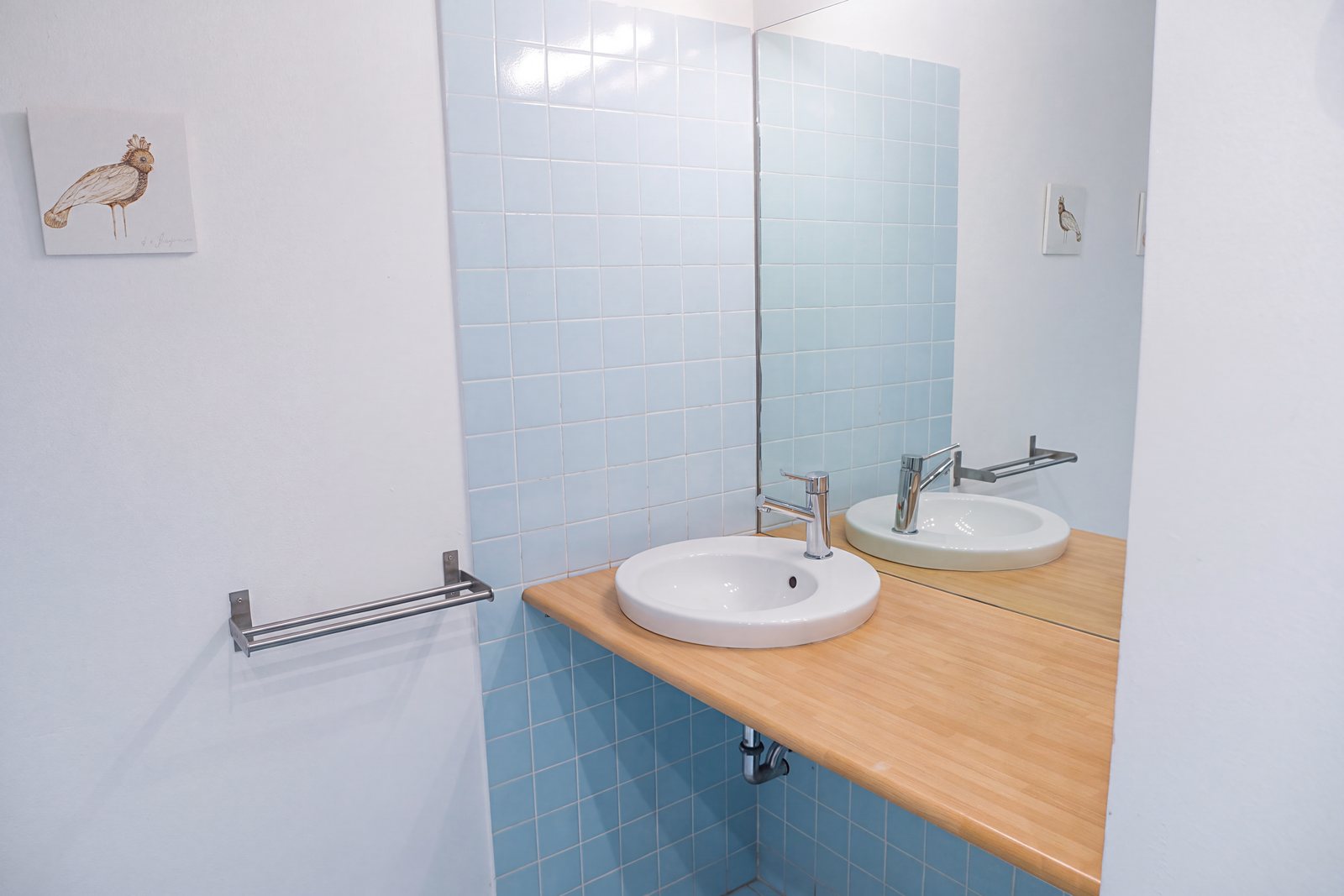Bad mit hellblauen Fliesen, rundem Waschbecken auf Holzplatte und großem Spiegel, Viale della Terza Armata, Triest