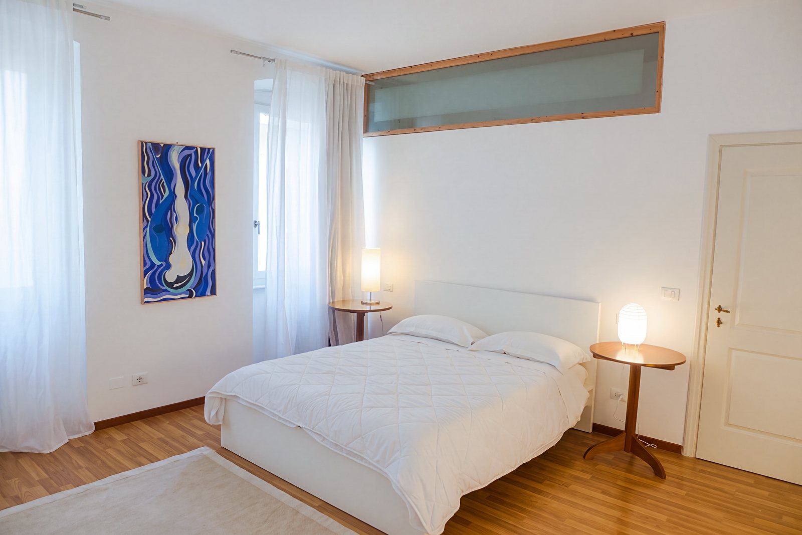 Schlafzimmer mit weißem Doppelbett, blauem Gemälde und zwei Fenstern mit Vorhängen, Viale della Terza Armata, Triest