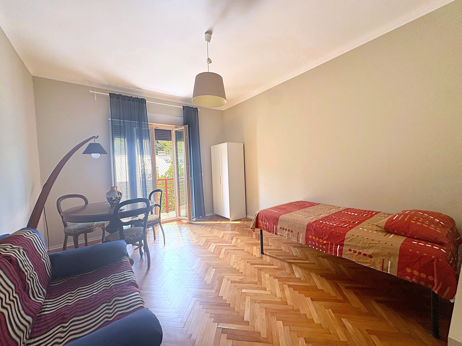 Stanza grande con divano, tavolo rotondo e letto singolo, porta-finestra sul balcone, viale XX Settembre, Trieste