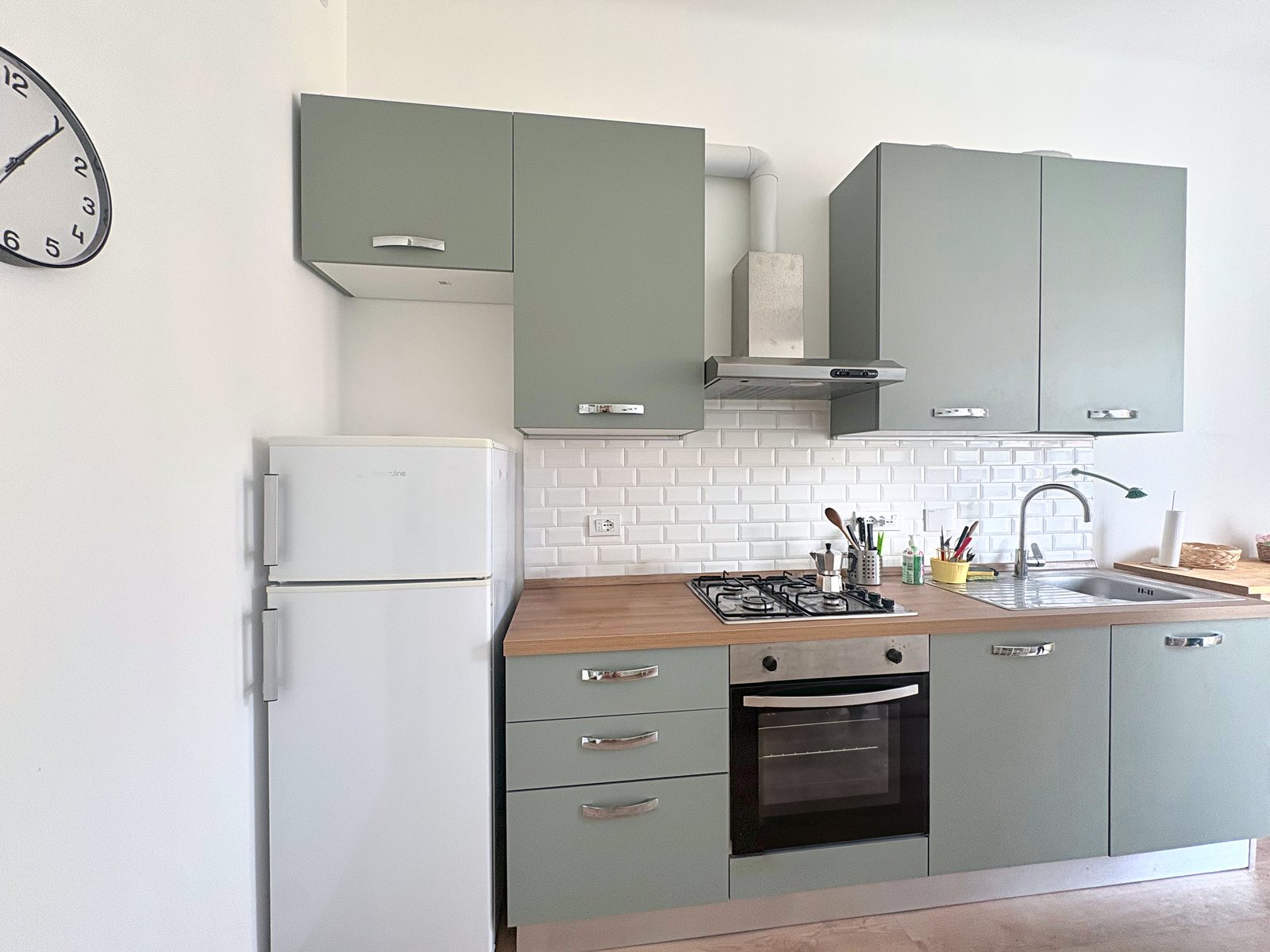 Cucina con mobili verde salvia, piastrelle diamantate bianche, piano a gas, forno e frigorifero, Trieste