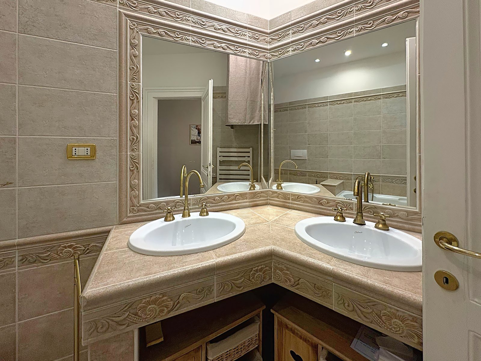 Bagno con doppio lavabo ad angolo, rubinetti in ottone e grande specchio decorato, via San Giorgio, Trieste