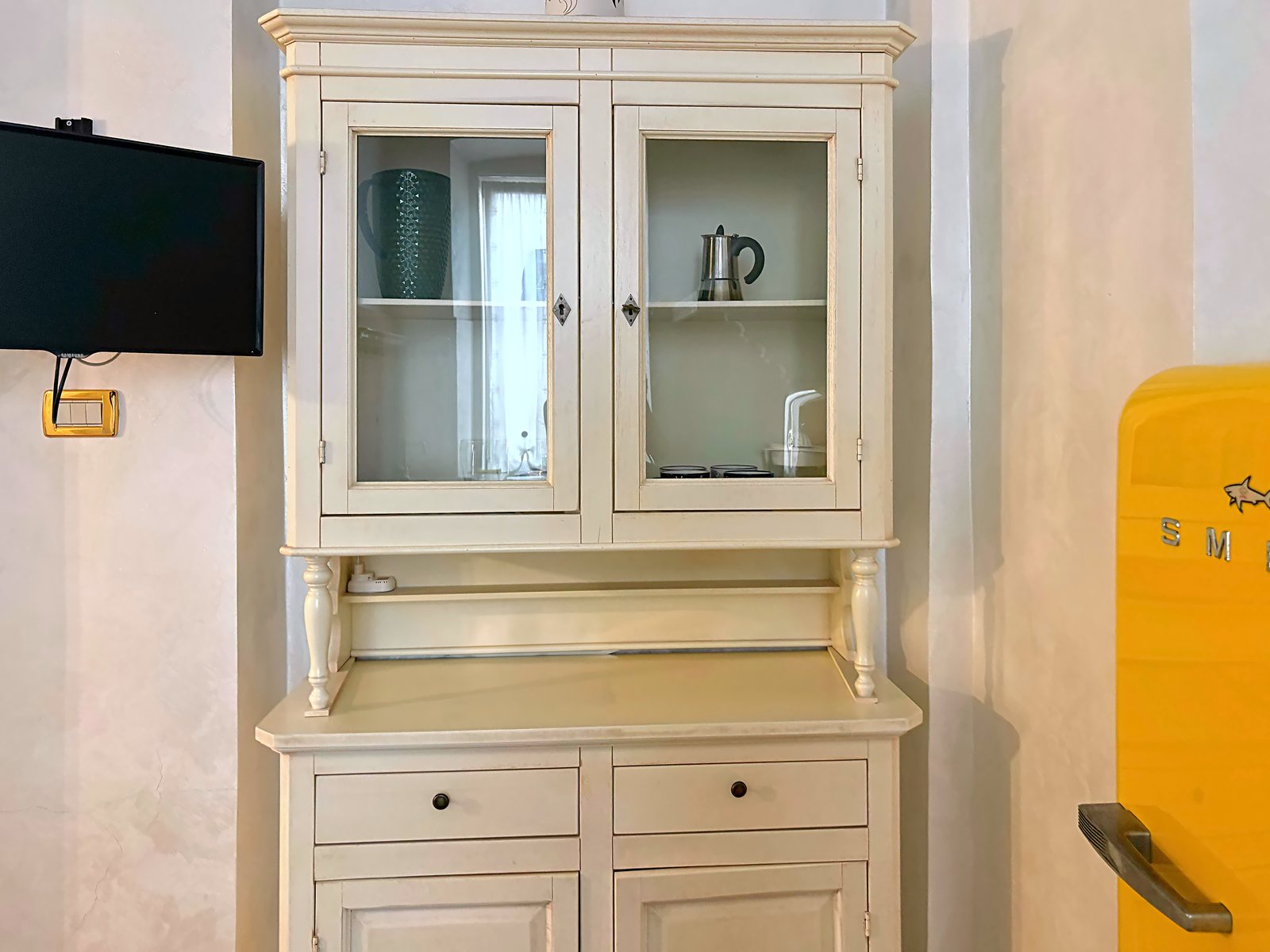 Credenza a vetrina color crema con TV a parete e frigorifero giallo in cucina, via San Giorgio, Trieste