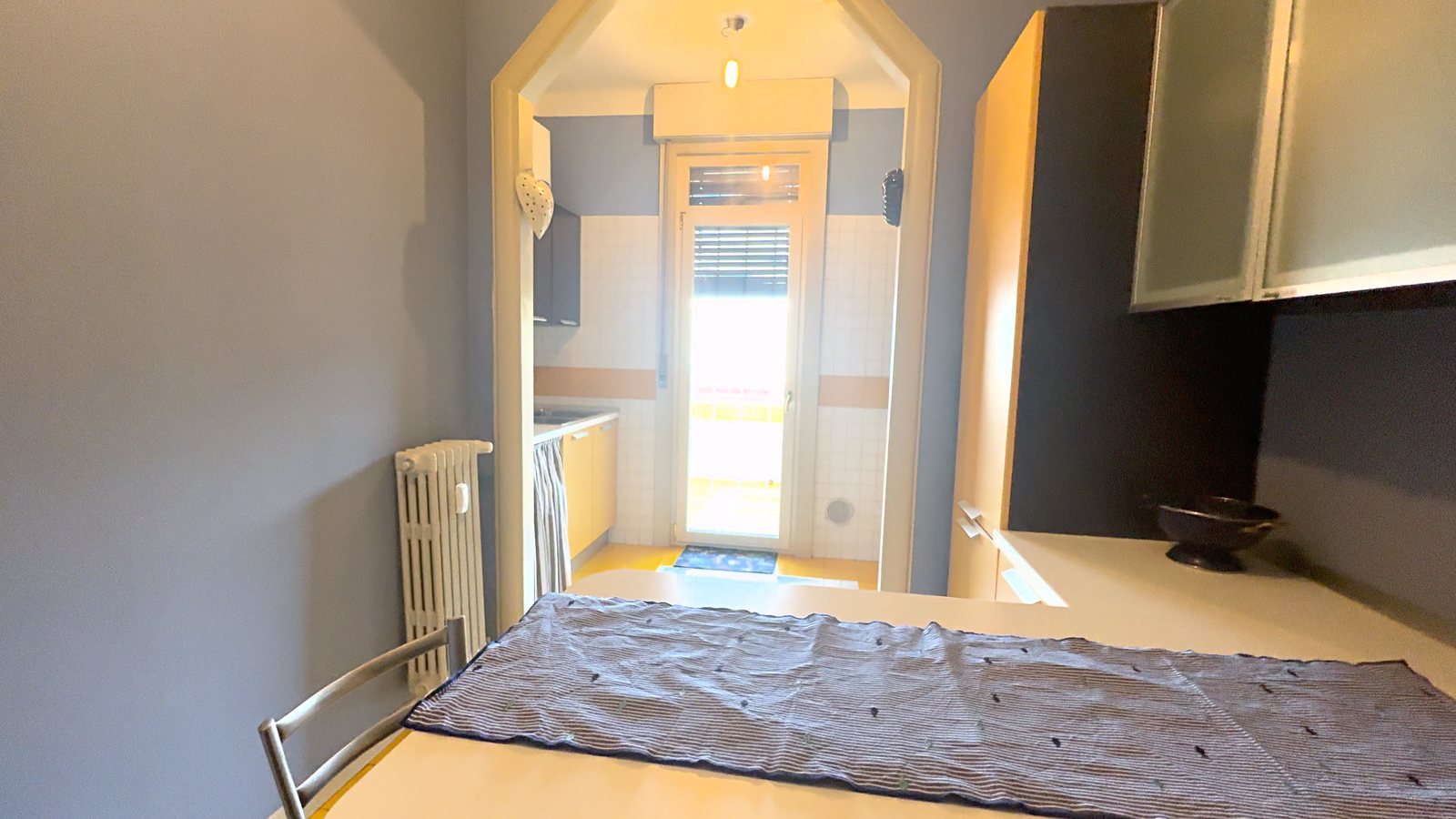 Kuhinja z jedilnim kotom, modrosivimi stenami, rumenimi omaricami in vrati na balkon, Via Belpoggio, Trst
