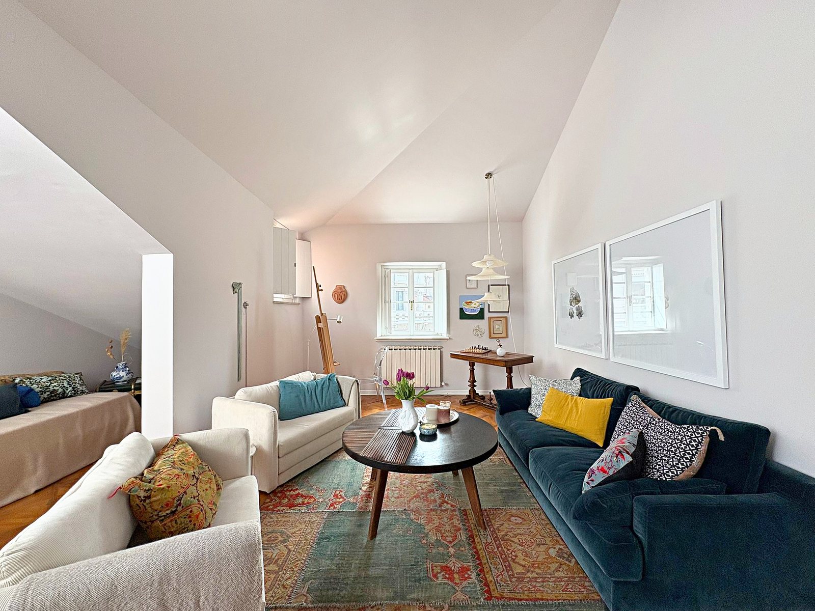 Attic living room with green velvet sofa, cream armchairs and window onto Piazza Goldoni, Trieste