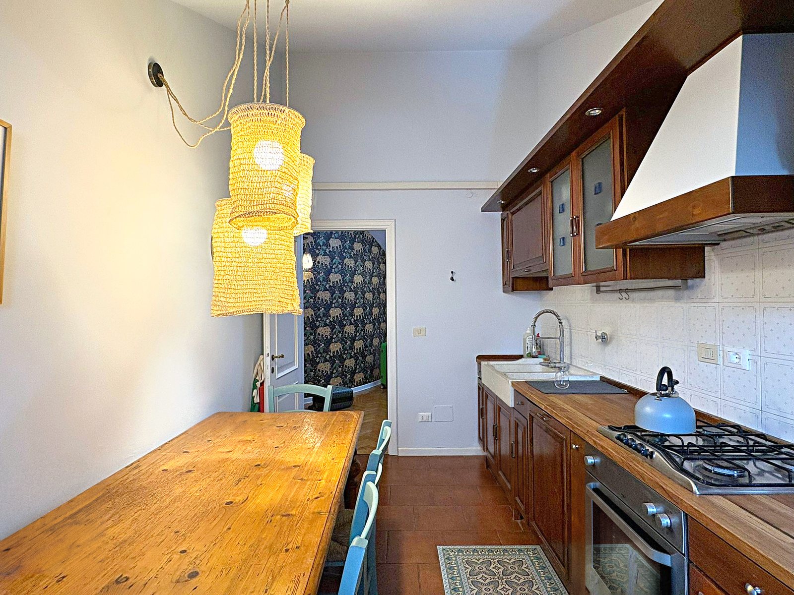 Cucina abitabile con tavolo lungo in legno, lampade in vimini e pensili scuri, mansarda in piazza Goldoni, Trieste