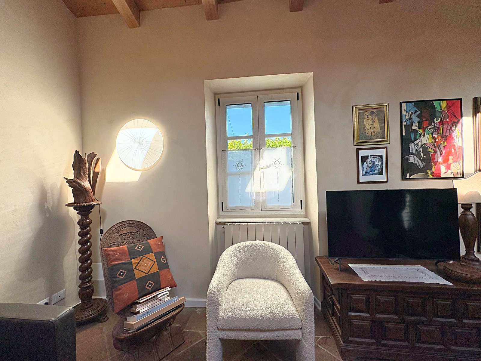 Wohnzimmerecke mit Bouclé-Sessel, Fernseher auf geschnitzter Truhe und Fenster, Steinhaus in Duino