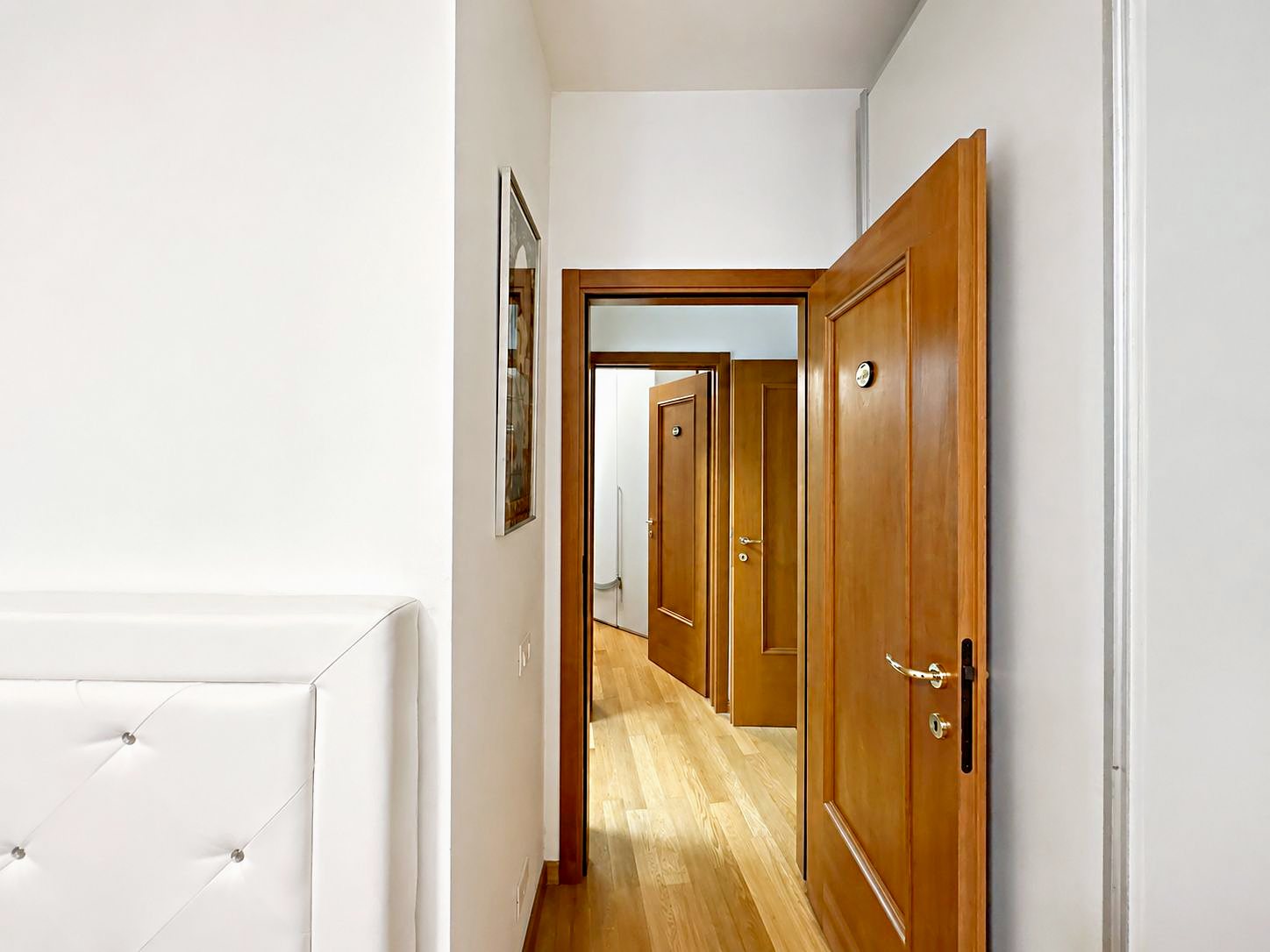 Camera verso la porta, con testiera imbottita e porte in legno sul disimpegno, Via del Trionfo, Trieste
