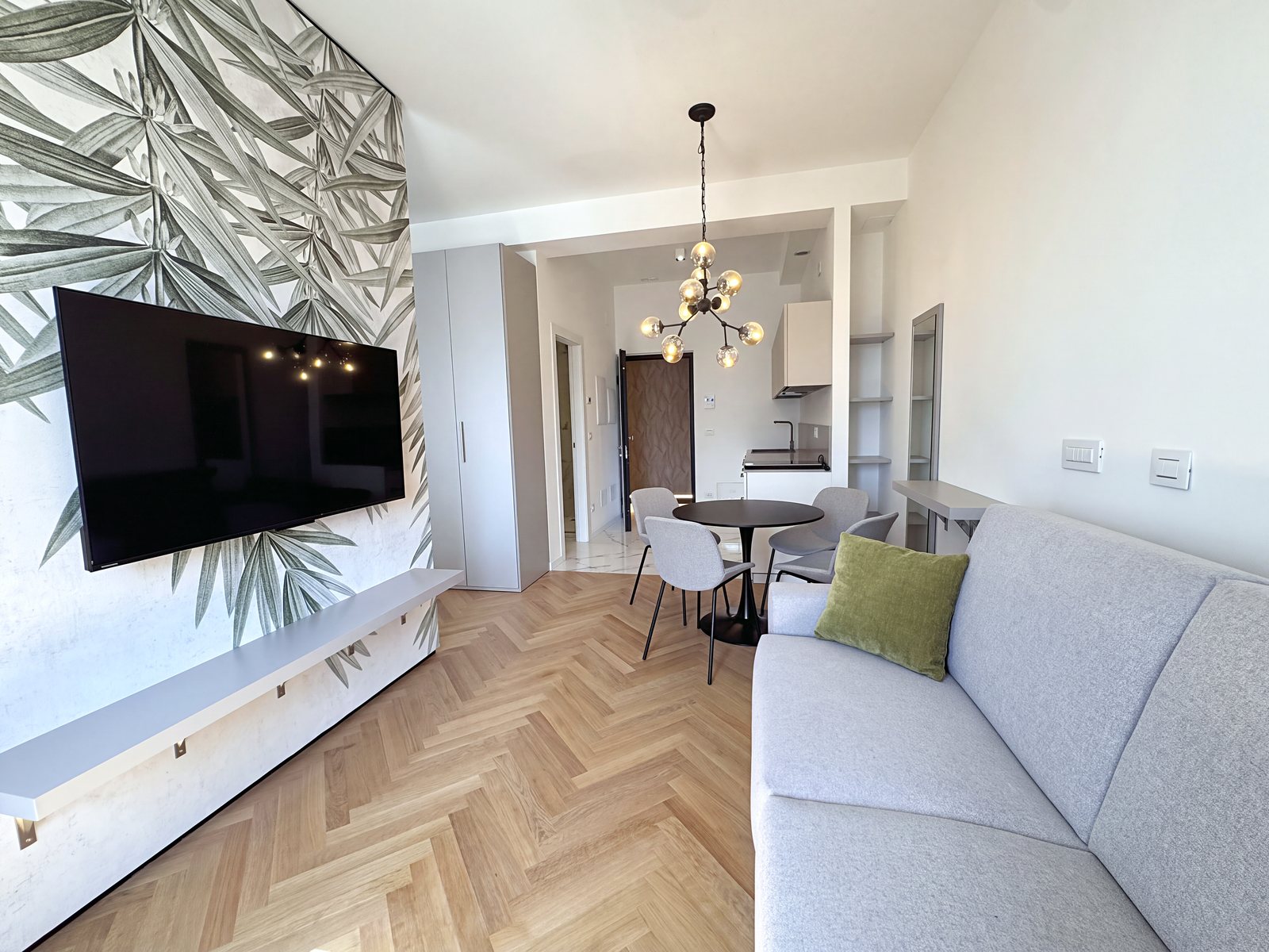 Living area with television on the leaf-pattern wall, sofa and kitchen towards the entrance, Via Carducci, Trieste