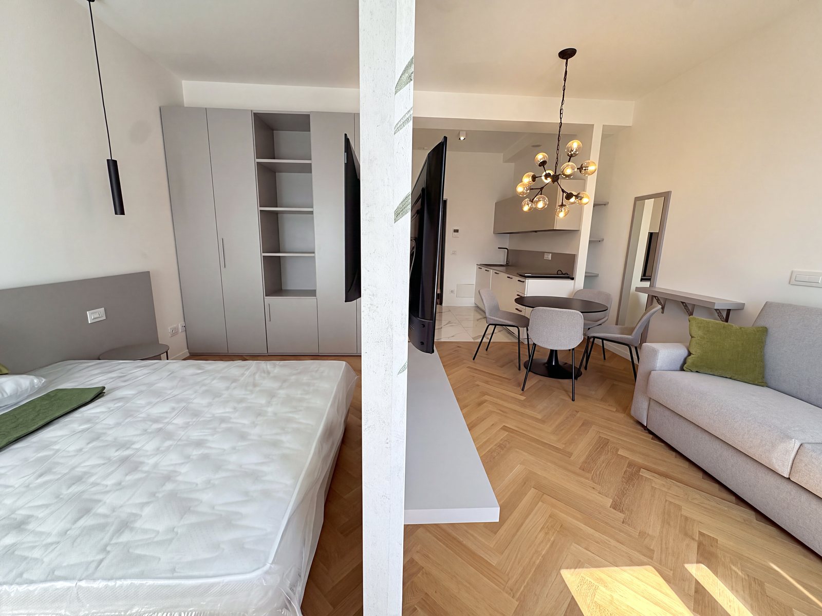 Sleeping area with bed and wardrobe, divided from the living area by a wall with the television, Via Carducci, Trieste