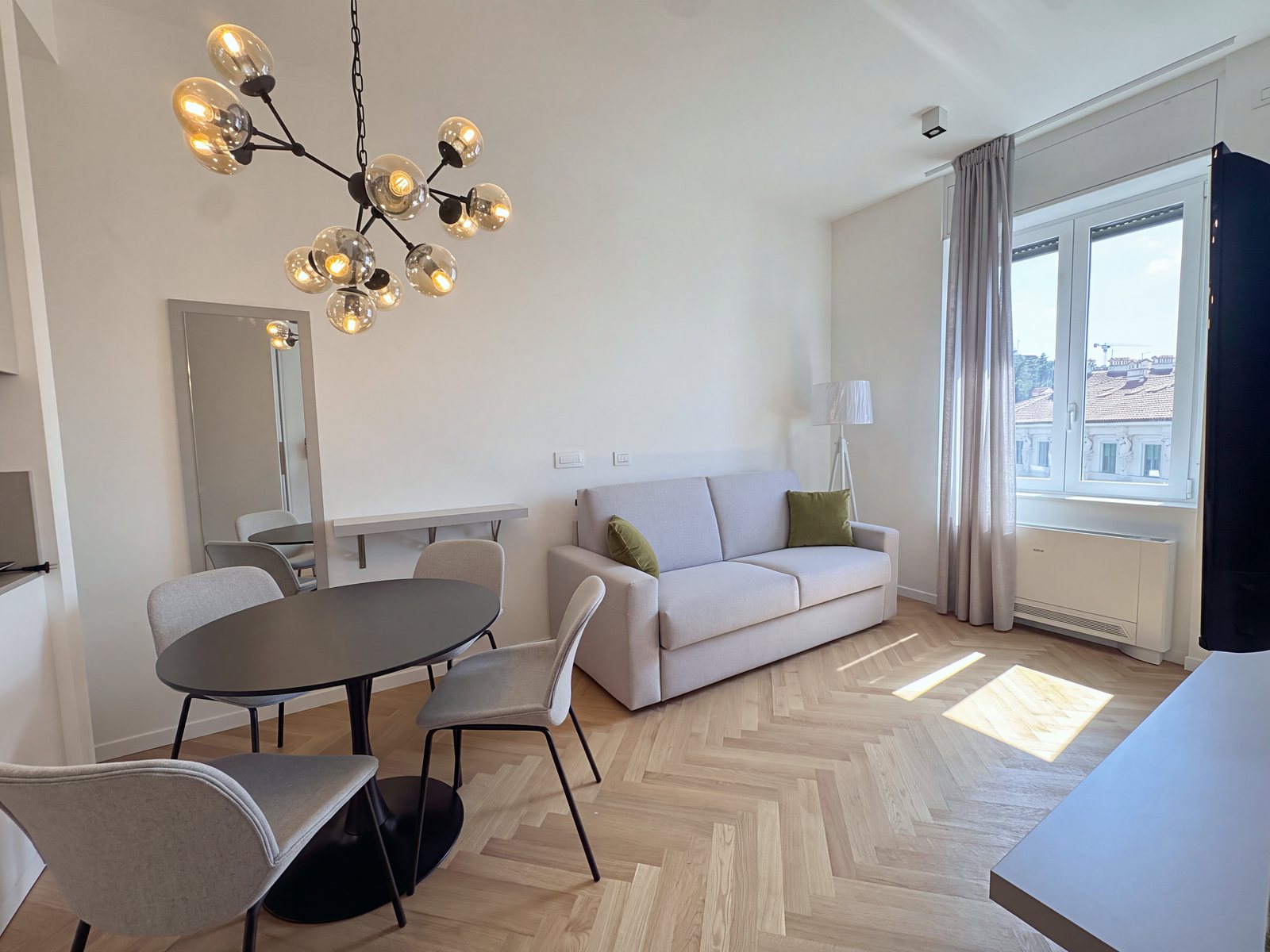 Living area with sofa, round table, chandelier and window over the rooftops, Via Carducci, Trieste