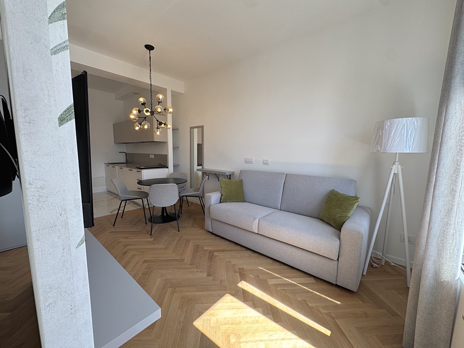Living area with grey sofa, floor lamp and kitchen in the background, Via Carducci, Trieste