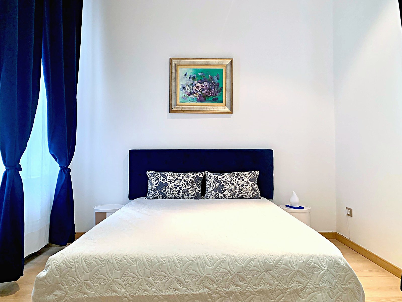 Camera matrimoniale con testiera blu notte, tende blu e quadro a fiori, Via XXX Ottobre, Trieste
