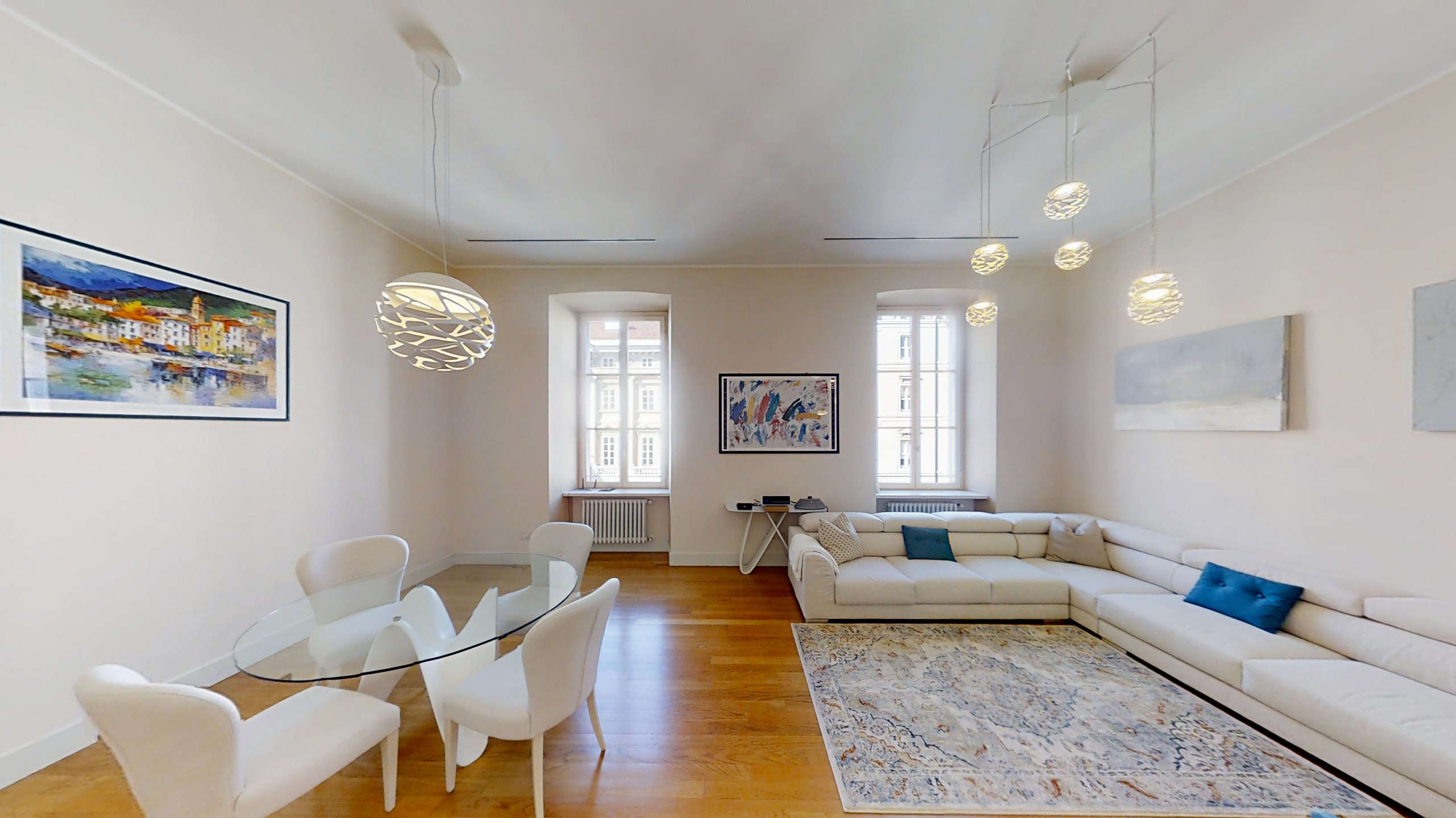 Wohnzimmer mit weißem Ecksofa, gläsernem Esstisch und zwei Fenstern, Palazzo Tergesteo, Triest