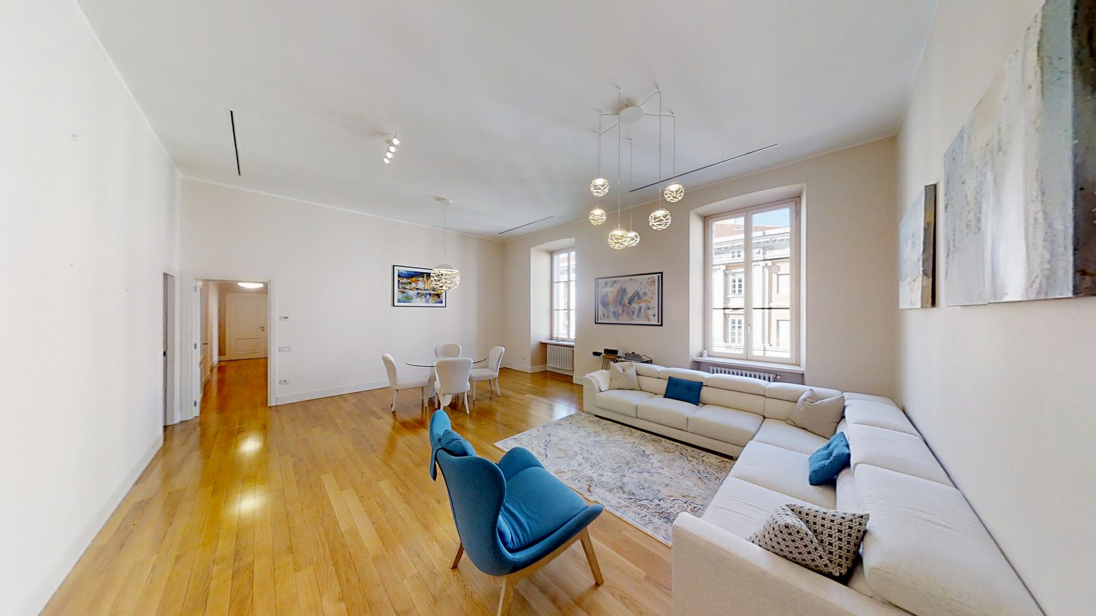 Langes Wohnzimmer mit blauem Sessel, weißem Ecksofa und Eichenparkett, Palazzo Tergesteo, Triest