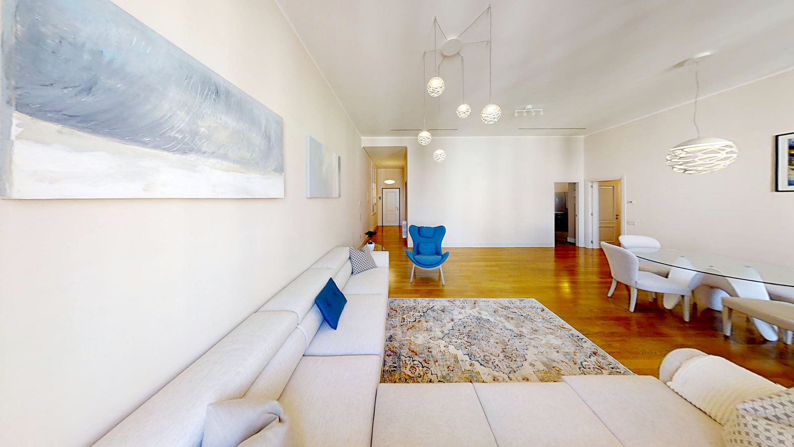 Wohnzimmer Richtung Eingang mit weißem Sofa, Teppich, blauem Sessel und Essbereich, Palazzo Tergesteo, Triest