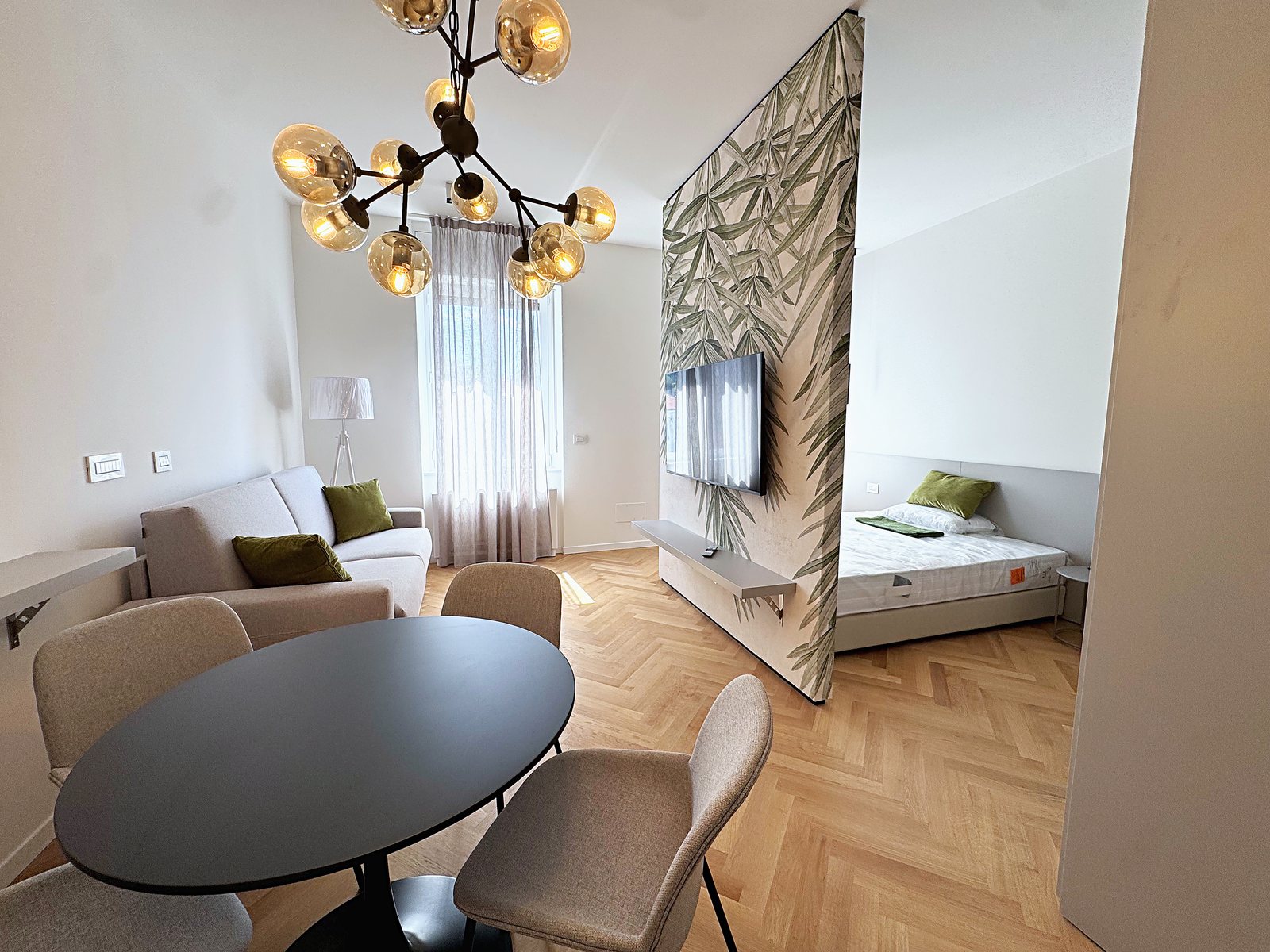 Living area with round table, sofa, chandelier and bed beyond the leaf-pattern wall, Via Carducci, Trieste