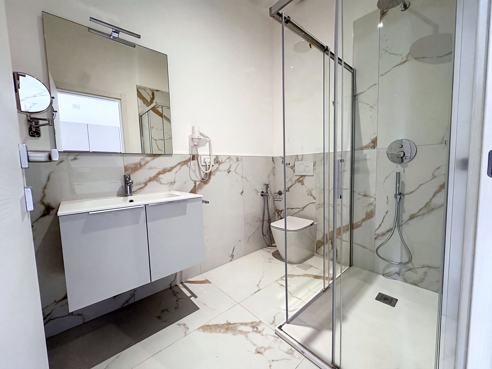 Bagno con box doccia in vetro, lavabo su mobile e rivestimento effetto marmo, via Carducci, Trieste