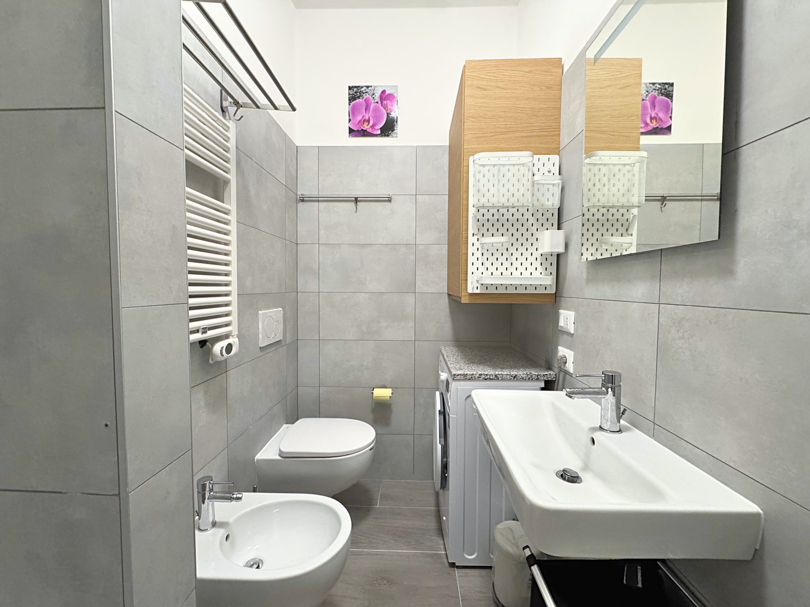 Bagno con piastrelle grigie, sanitari sospesi, scaldasalviette, lavabo e lavatrice, via del Lavatoio, Trieste