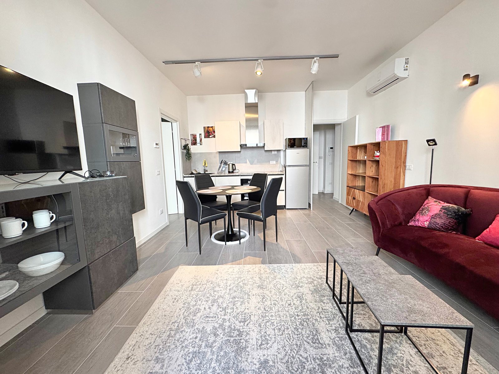 Open-plan living room with burgundy velvet sofa, TV and galley kitchen at the back, Borgo Teresiano, Trieste