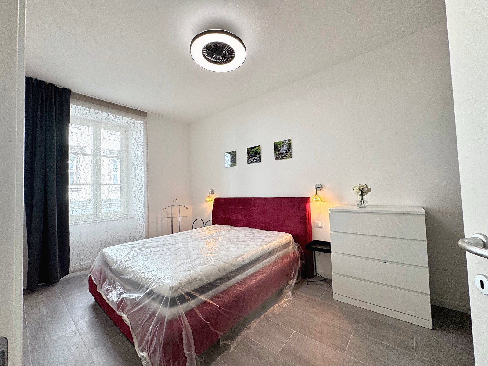 Camera matrimoniale con testiera imbottita bordeaux, comò bianco e finestra con tende, Borgo Teresiano, Trieste