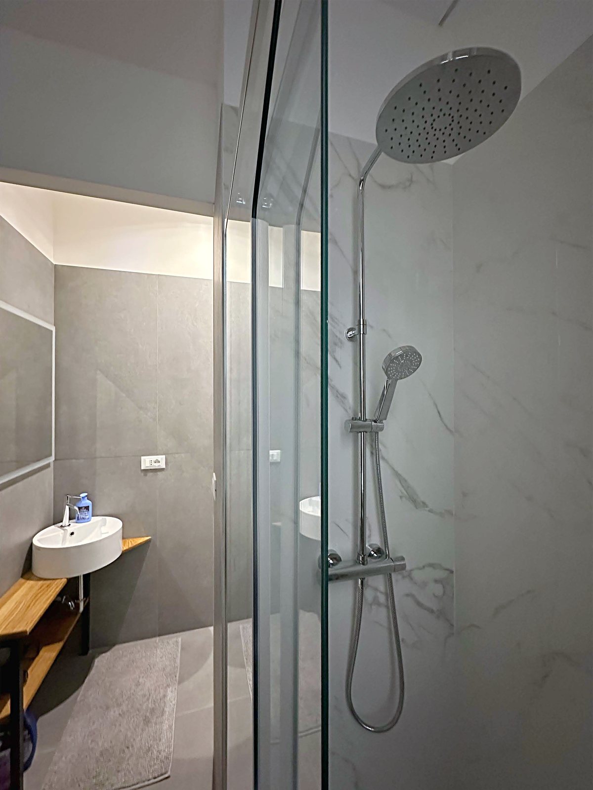 Dusche mit Regenbrause und Wand in Marmoroptik, rundes Waschbecken dahinter, Via della Madonnina, Triest