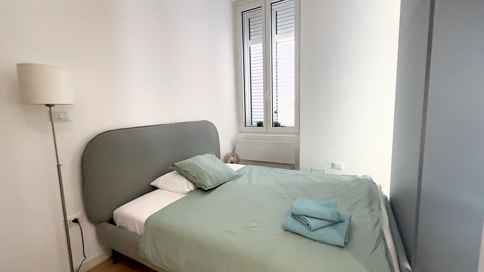 Schlafbereich hinter der Trennwand: Doppelbett, Stehlampe und Fenster, Via della Madonnina, Triest
