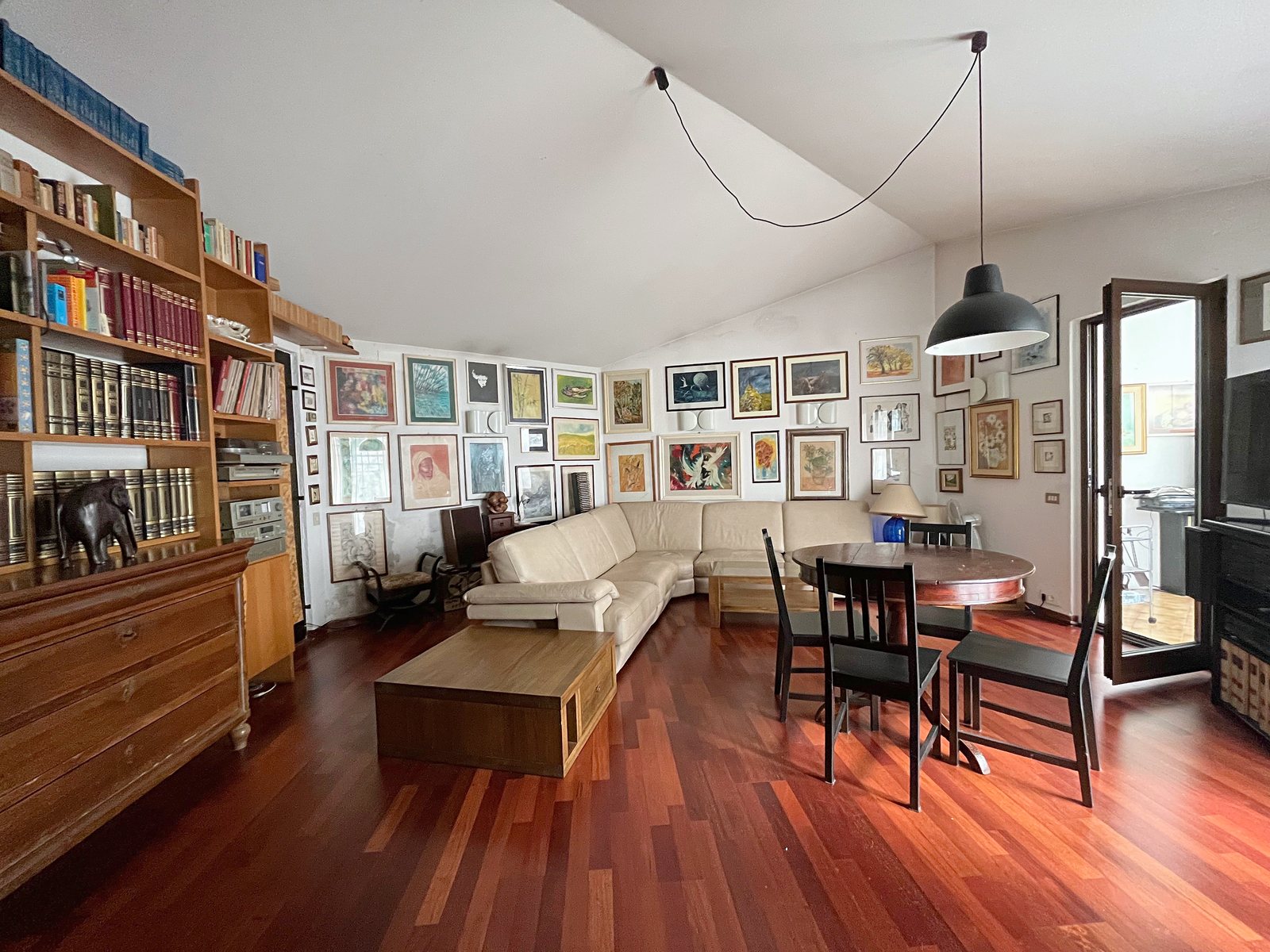 Living room with parquet, corner sofa, bookcase and a wall of paintings, Borgo Grotta Gigante, Sgonico, Trieste Karst