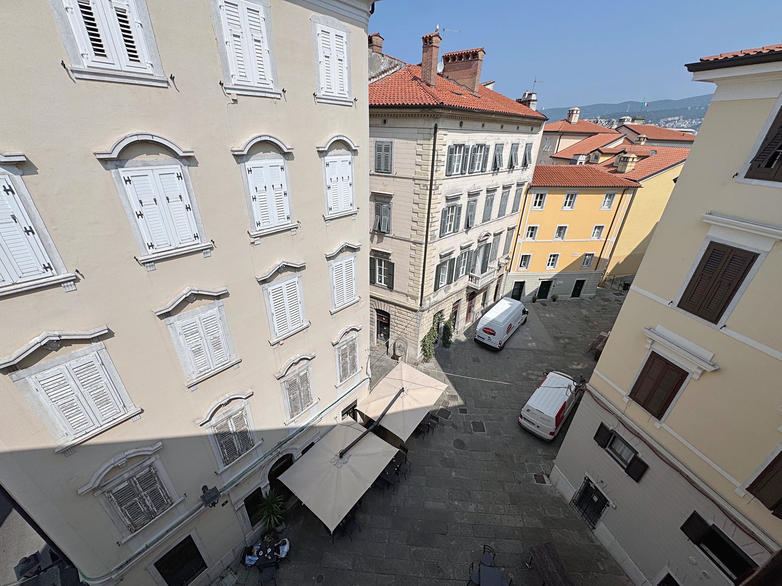 Pogled skozi okno na trg Piazzetta Barbacan in stavbe starega mestnega jedra, Trst