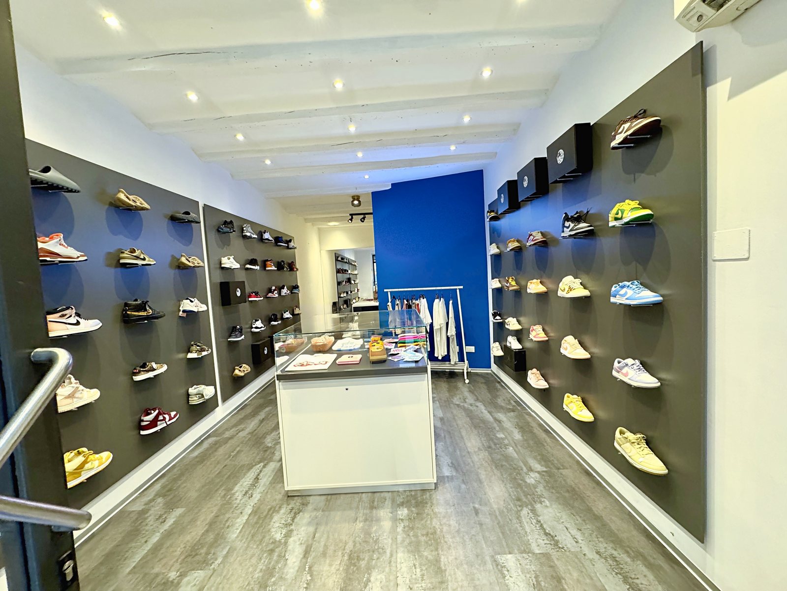Locale commerciale in via San Spiridione, Trieste: spazio di vendita con travi bianche e faretti, visto dall'ingresso