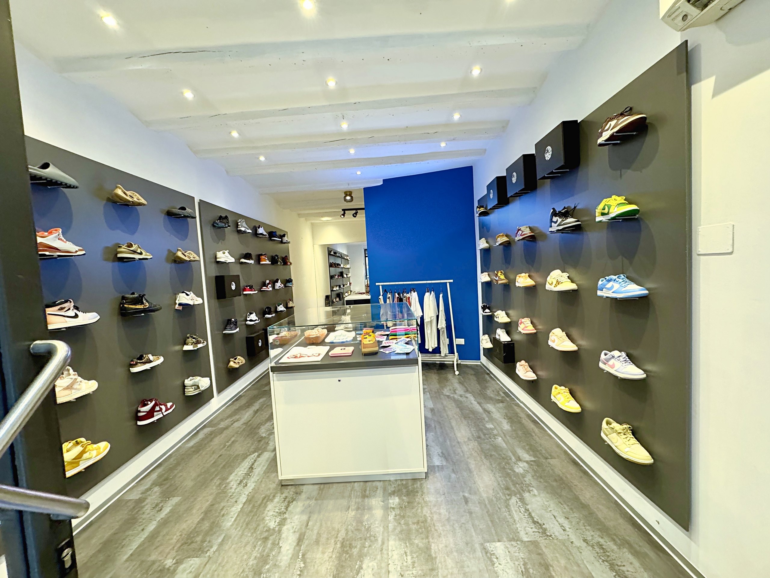 Locale commerciale in via San Spiridione, Trieste: spazio di vendita con travi bianche e faretti, visto dall'ingresso